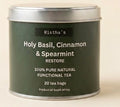A dark green metal tin of Ristha's Holy Basil, Cinnamon & Spearmint Restore tea, set against a solid light beige background.